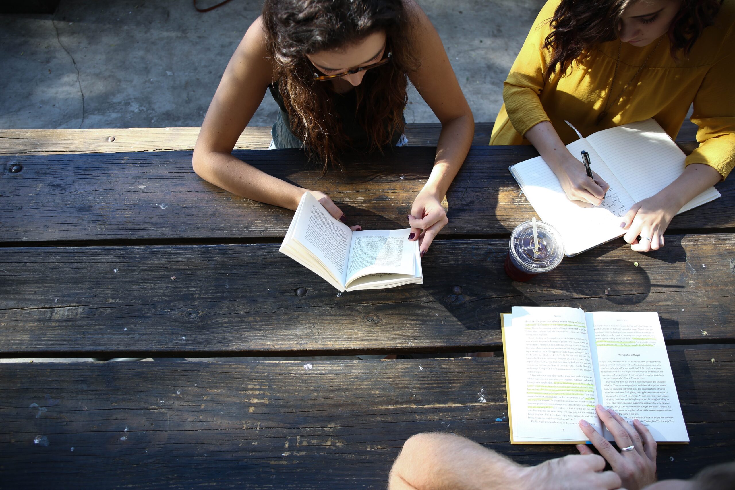three people viewed from above at an outdoor table reading and writing in notebooks.