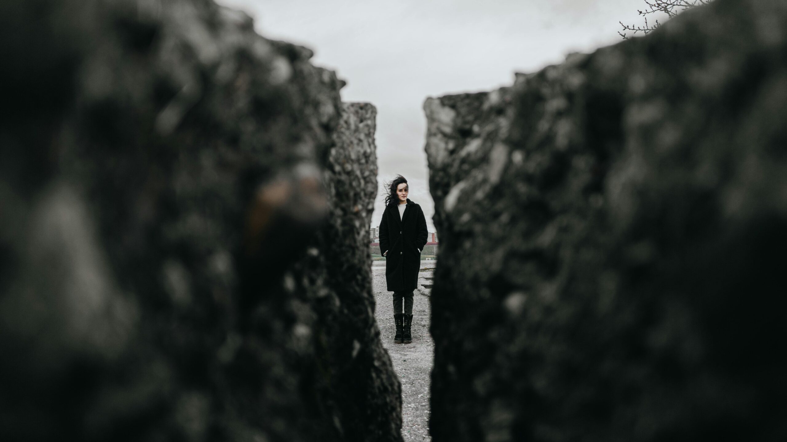 a person with long hair waving in the wind stands in the distance. The viewer looks at them through a gap between two rocks.