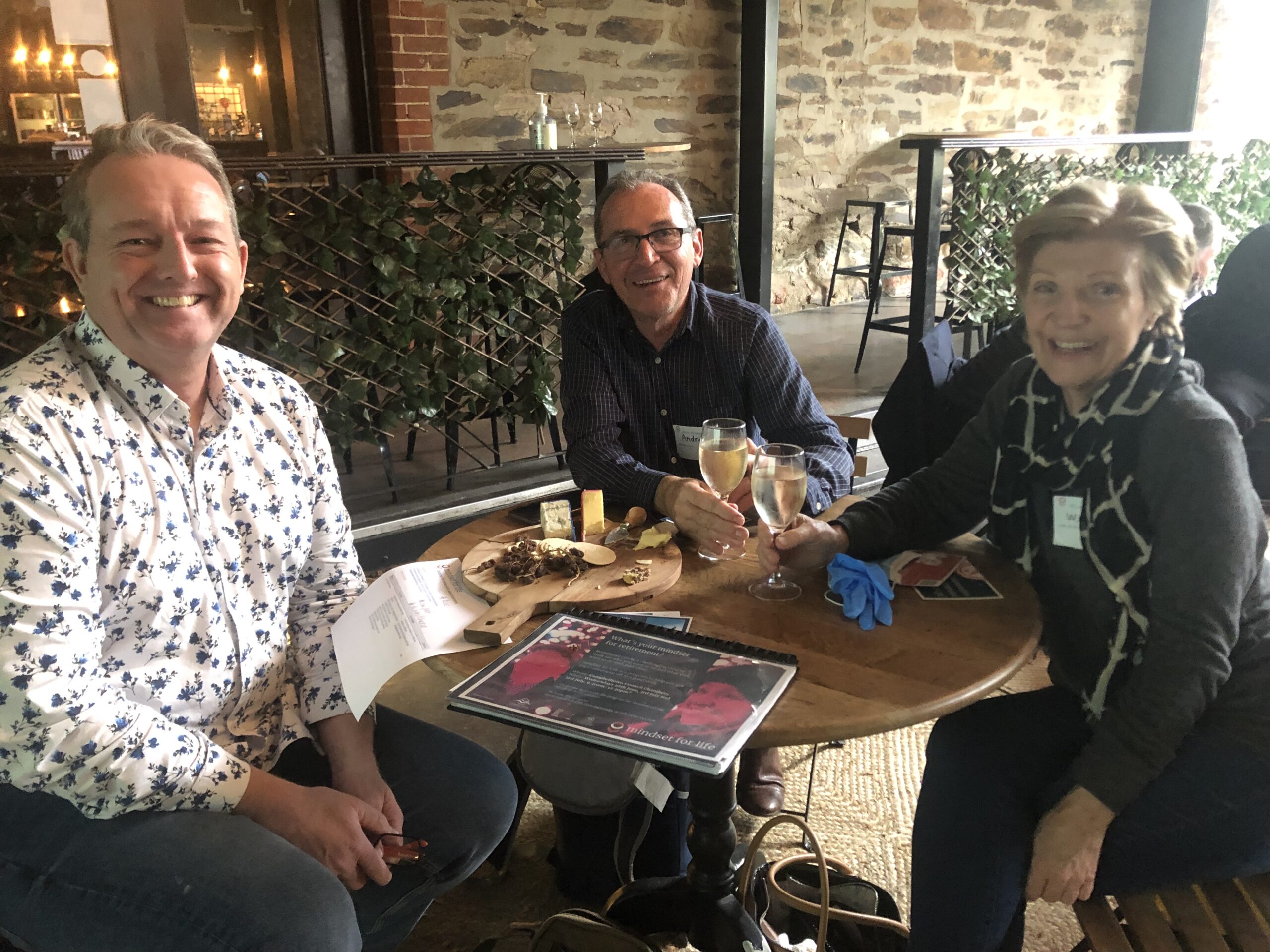 Two men and a woman smiling at the camera sitting round a cafe table.