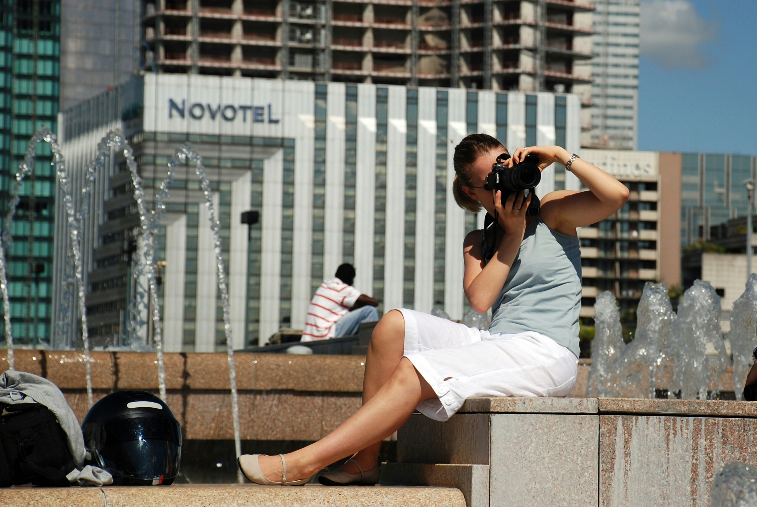 woman in white shorts with a camera held up to her face in from of a hotel